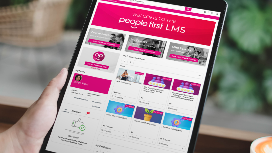 Hand holding a tablet device with the People First LMS dashboard on the screen