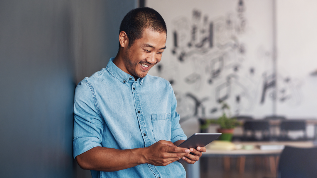 Young man casually leaning against wall looking at People First platform on tablet device