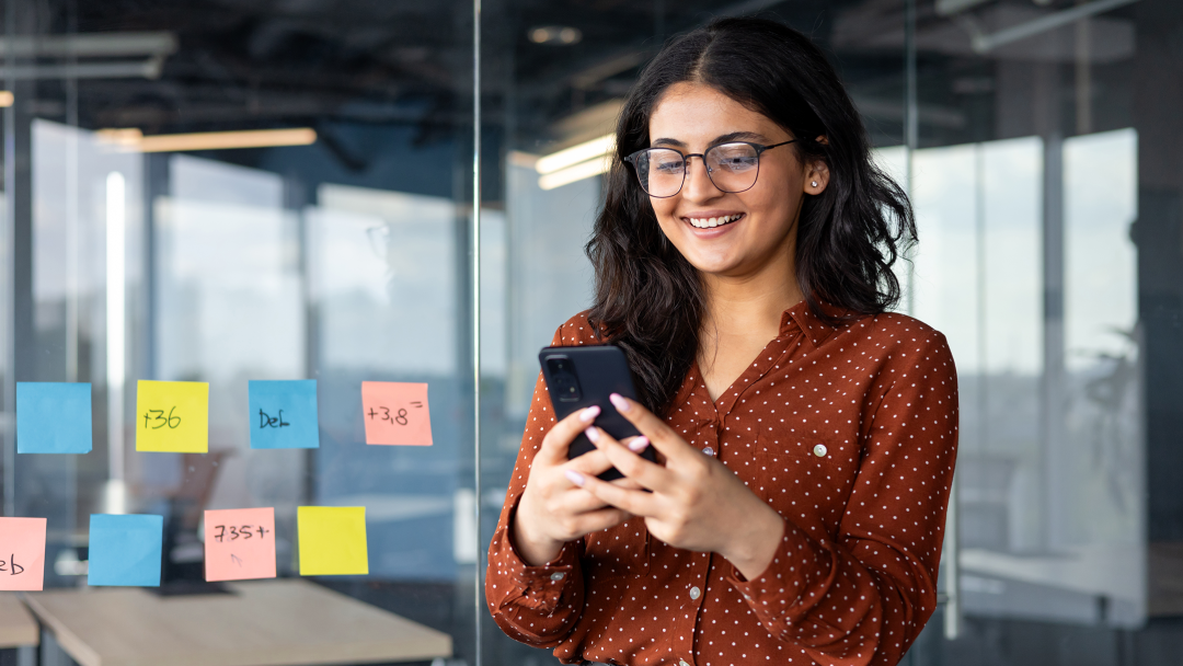 Young female stood in office looking at People First platform on mobile device
