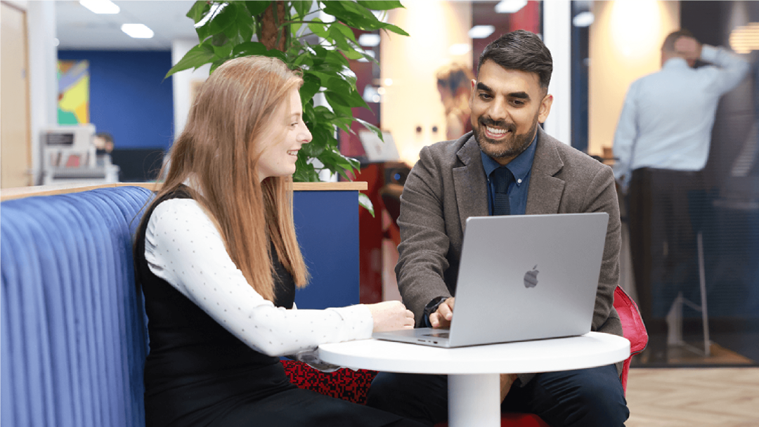 Colleagues discussing work while collaborating on a laptop