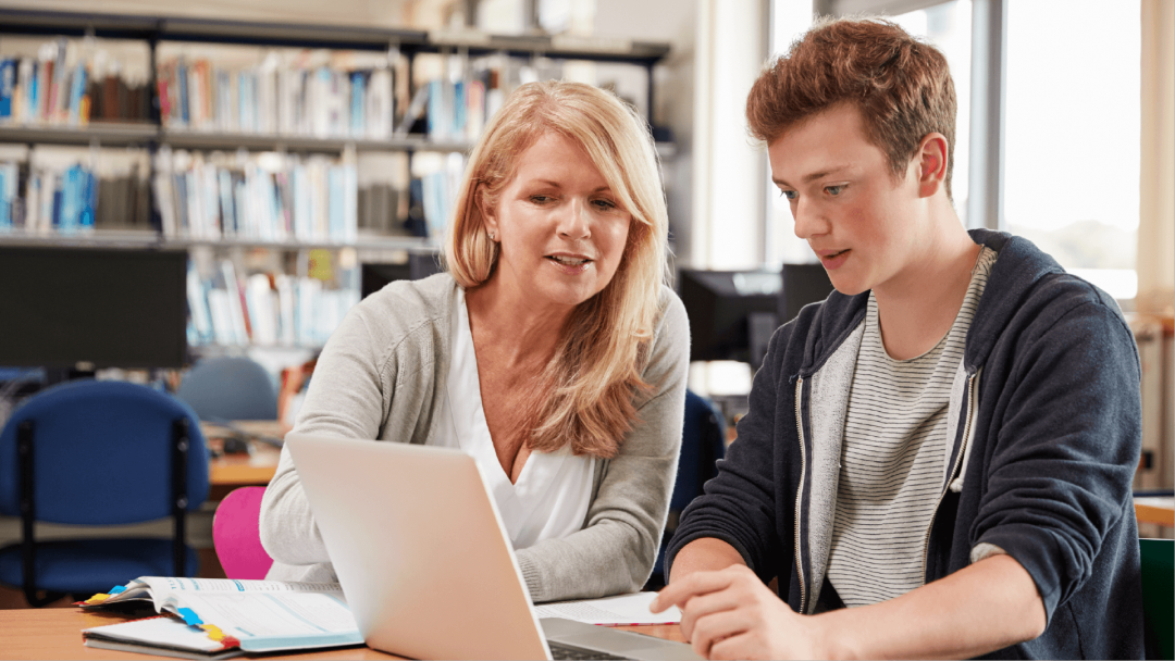 Teacher supporting a student while reviewing work on a laptop