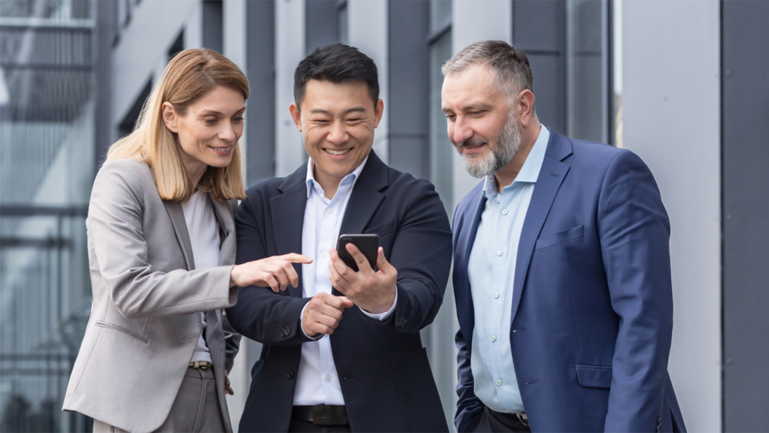 Three colleagues looking at a smartphone together during a discussion outside an office building
