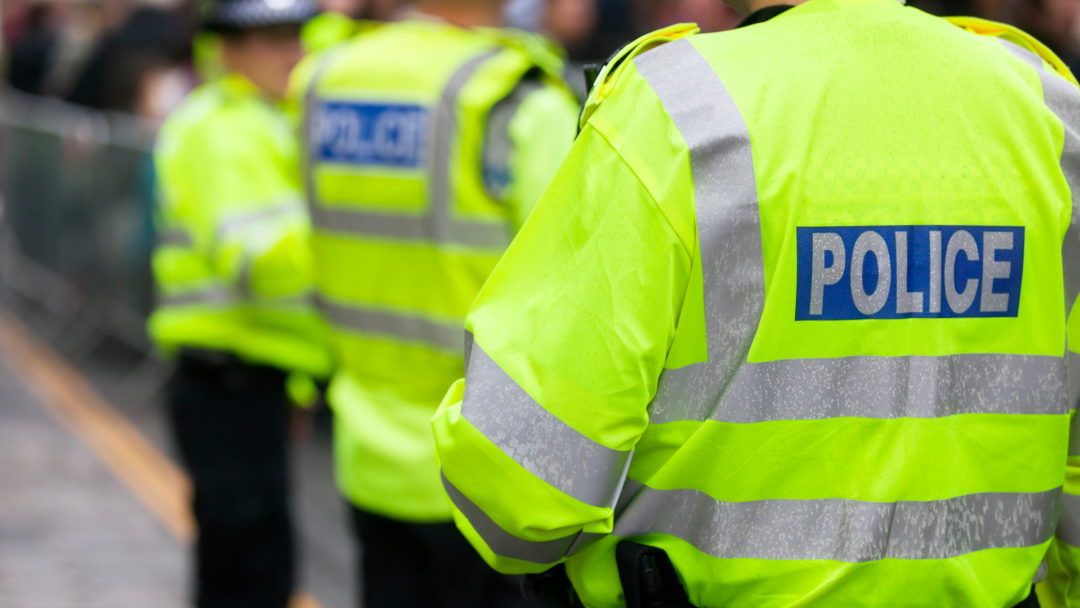 Police officers wearing bright yellow reflective vests, with "POLICE" visible on the nearest officers back.