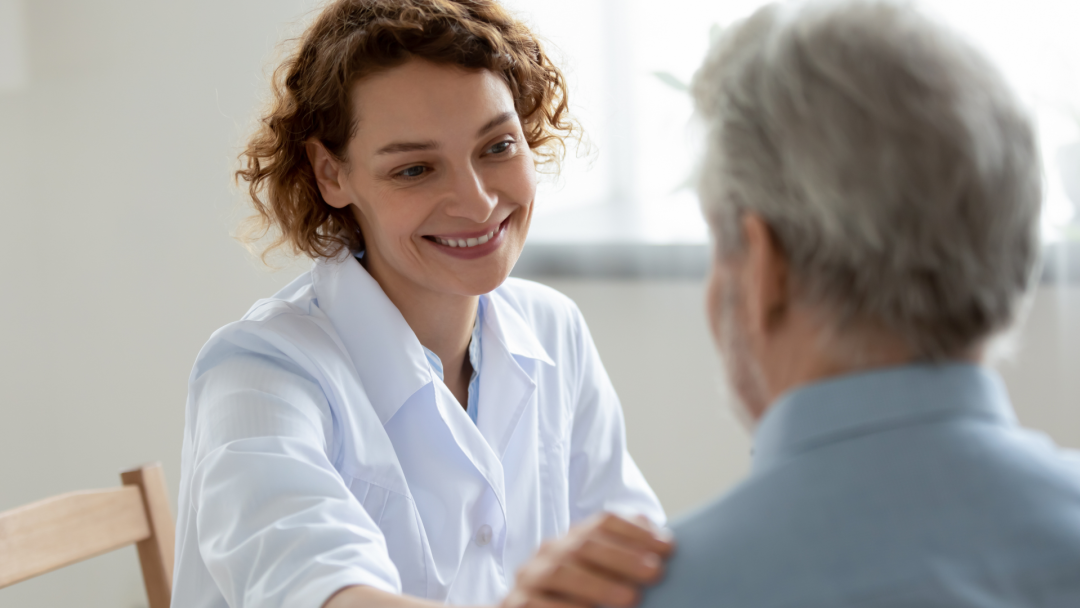 Smiling healthcare worker speaks with an older adult in a bright room.