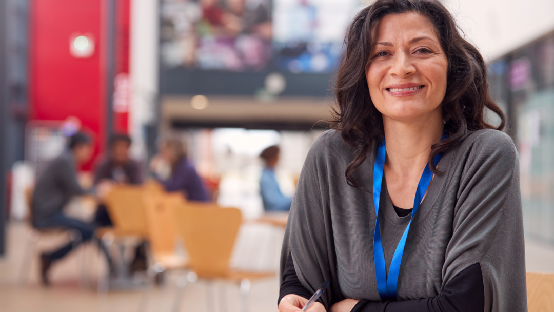 A woman smiling with a notebook and a tablet in an educational setting