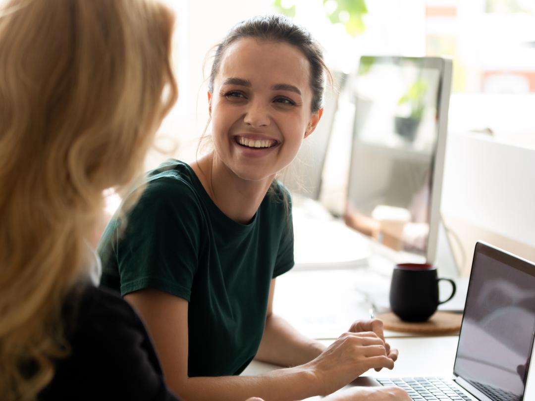two women chatting and smiling in front of a laptop