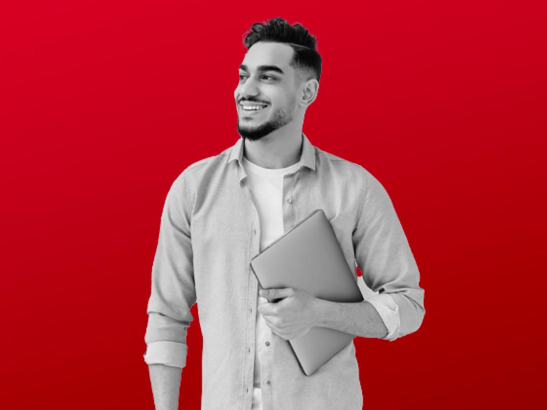 A man holding a laptop, looking to the side smiling.