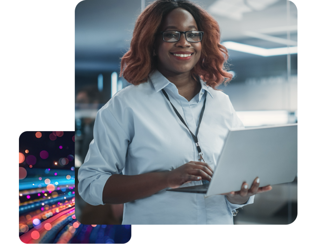 A lady stood in an office, holding a laptop smiling. 