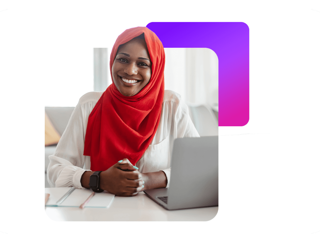 a lady sat down wearing a headscarf, working on a laptop smiling.
