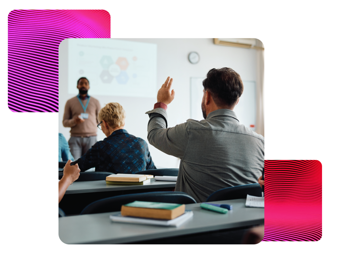 Classroom with 3 people. Man at the back has his hand up