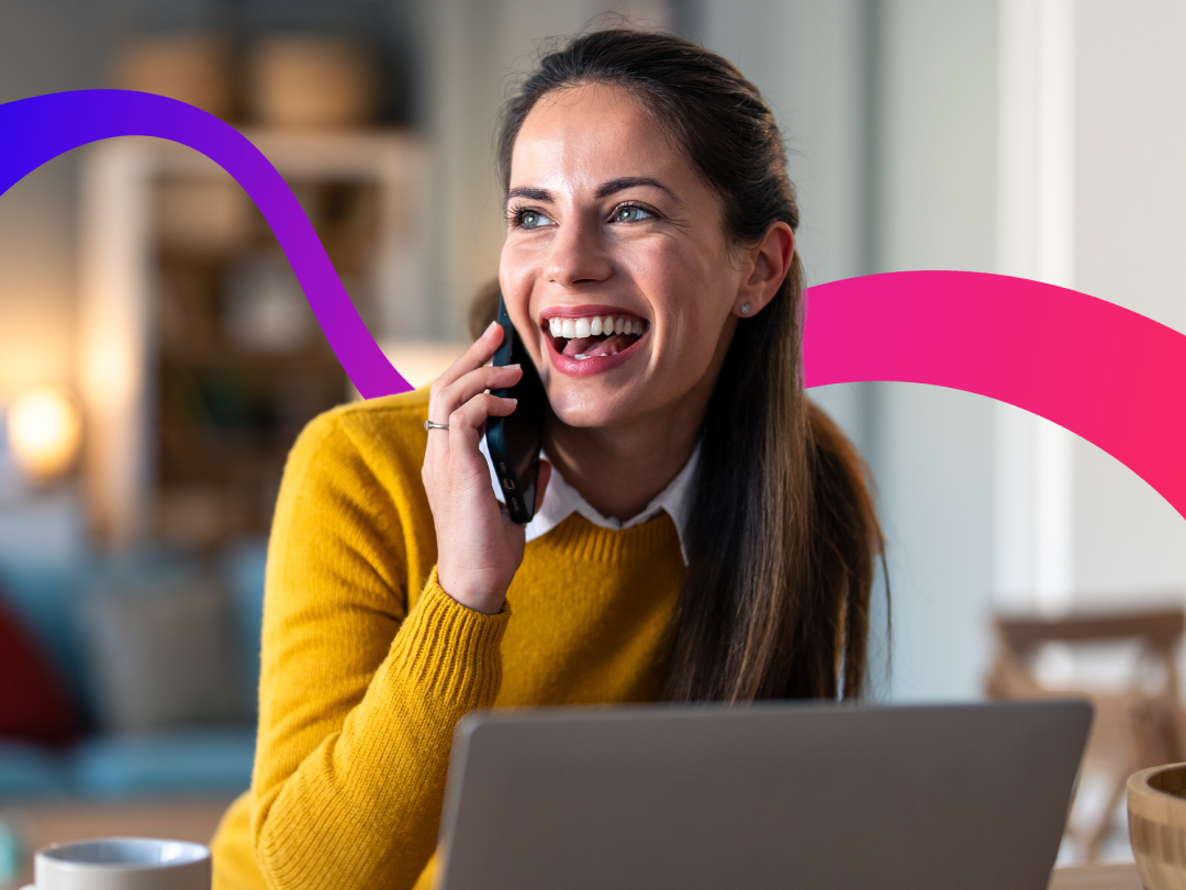 Woman on phone with laptop in front of her, looking into the distance and laughing.
