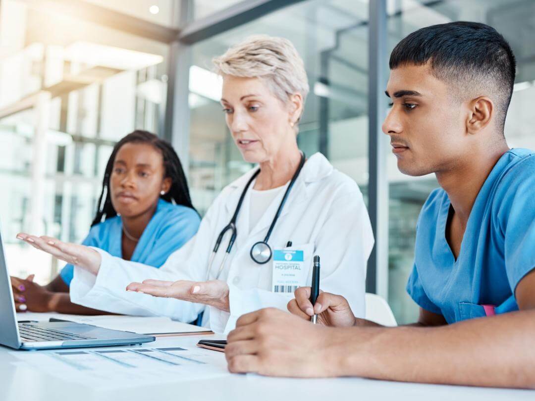Three doctors one man and two women sat around a laptop
