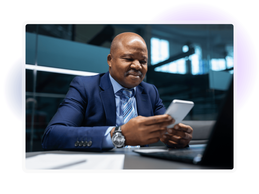 Business professional using a smartphone while seated at a desk with a laptop