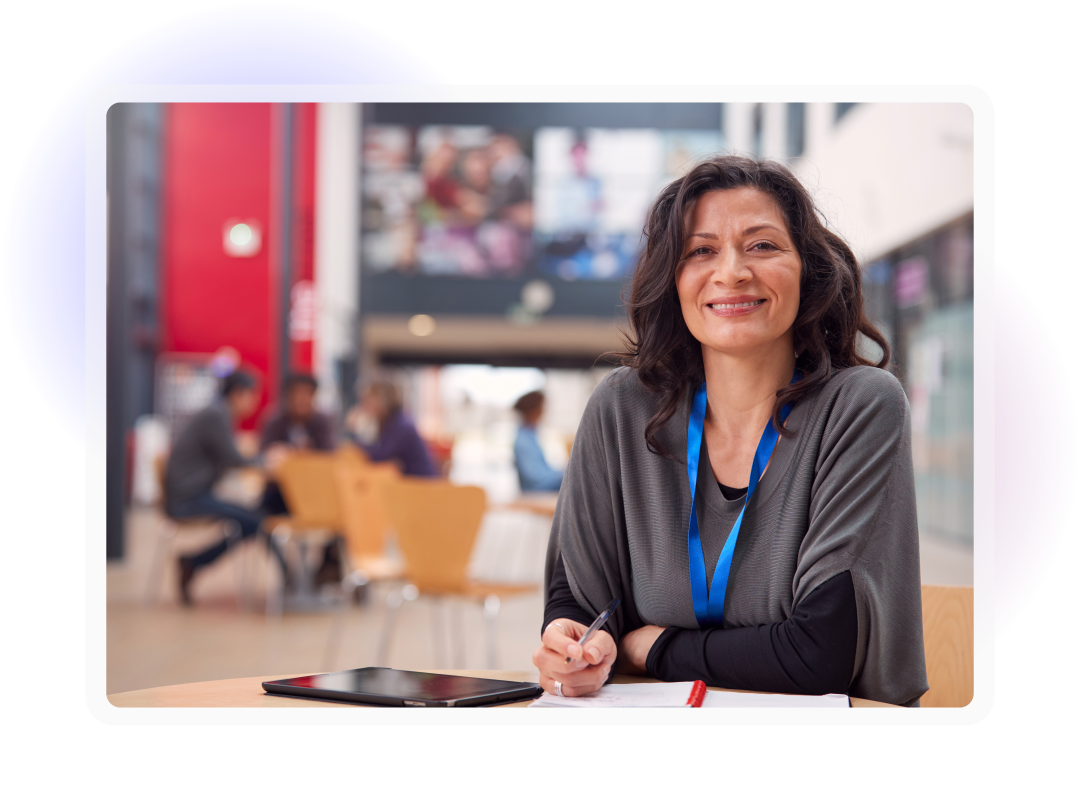 Staff member smiling while writing notes at a table in a modern education or campus environment