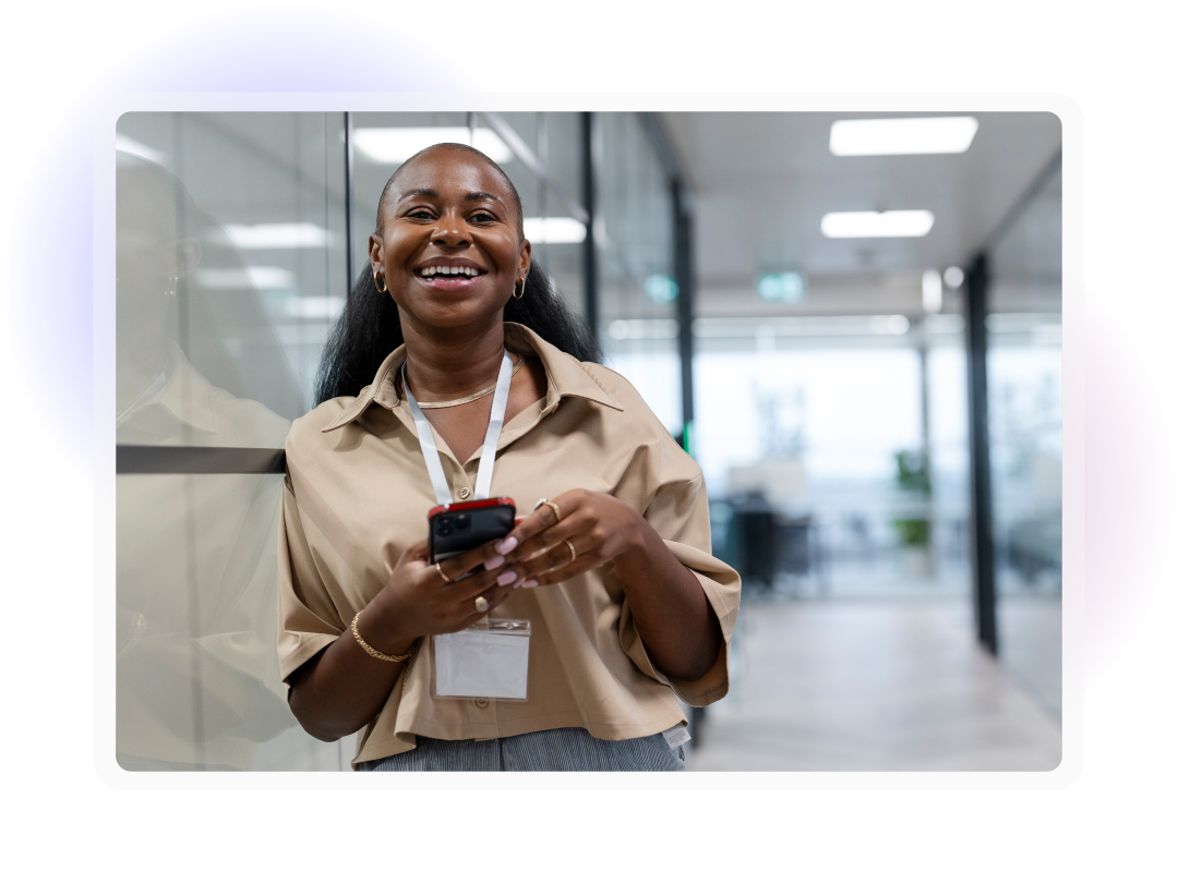 Employee smiling while using a smartphone in a modern office corridor