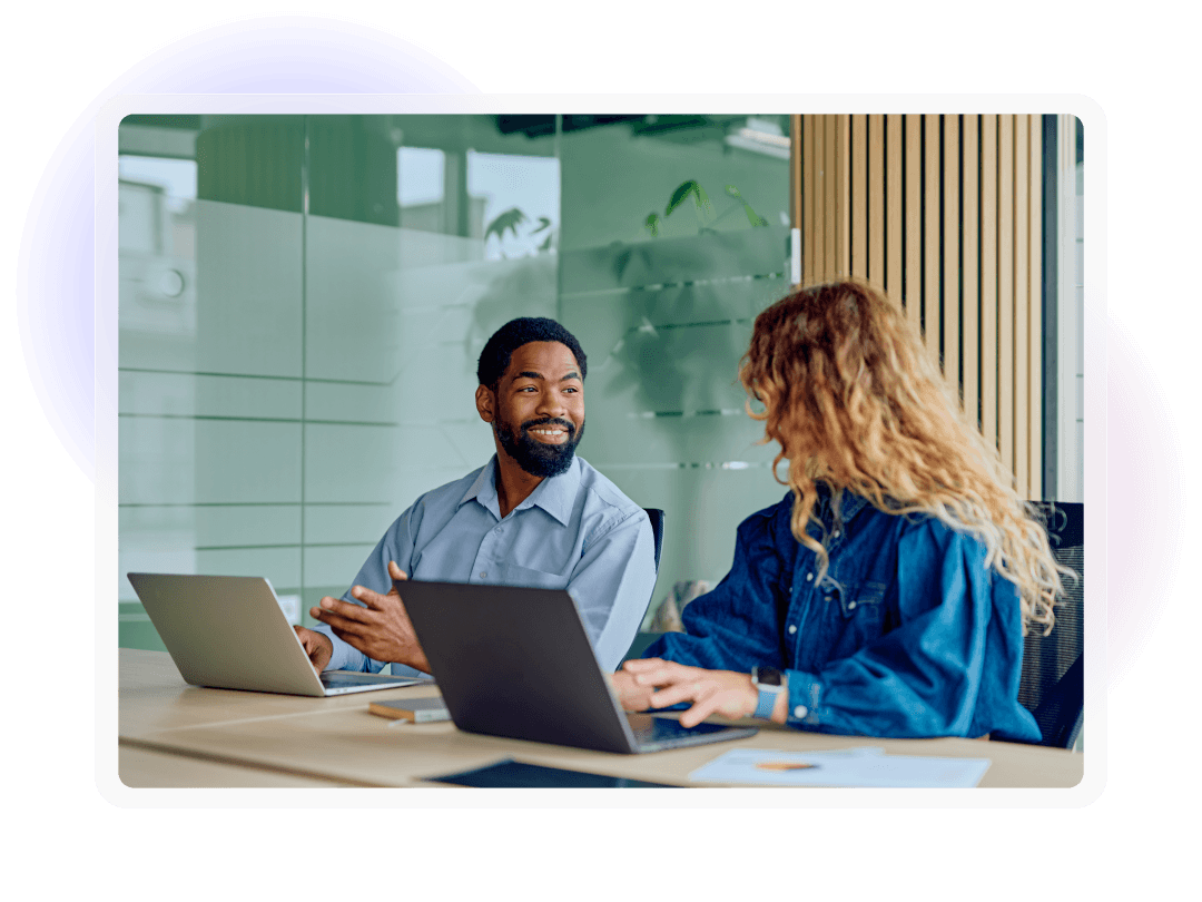 Two colleagues discussing work together at a table with laptops