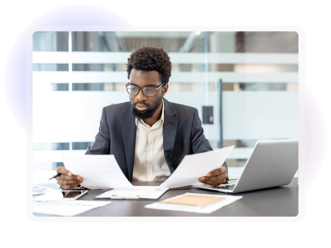 Employee reviewing printed documents beside a laptop at an office desk