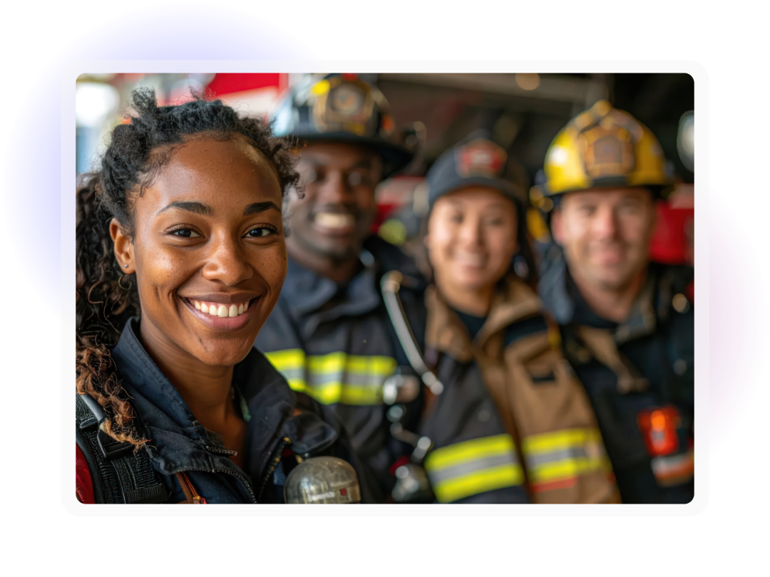 Smiling woman firefighter in the foreground, with three firefighters standing behind her inside a fire station.