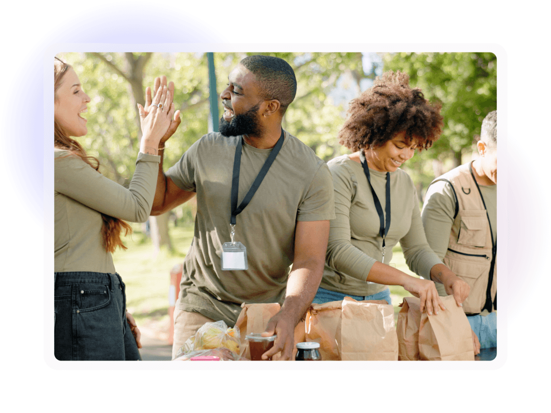 Four volunteers prepare food parcels outdoors as two people high-five.